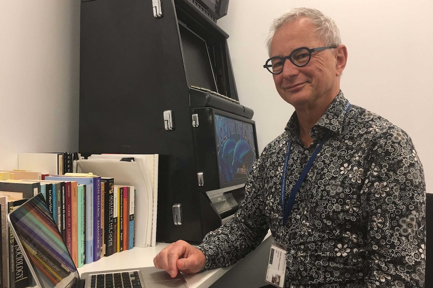 Dr Charles Livingstone adjusts books at his desk in his office.