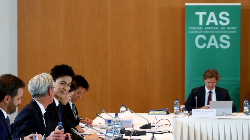 Sun Yang smiling and talking to a man in a suit while seated a the Court of Arbitration for Sport.