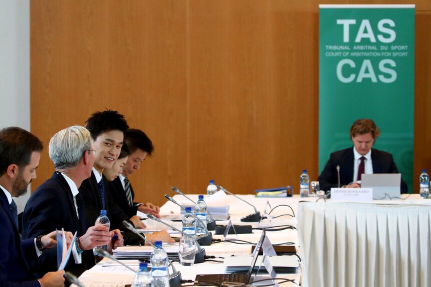 Sun Yang smiling and talking to a man in a suit while seated a the Court of Arbitration for Sport.