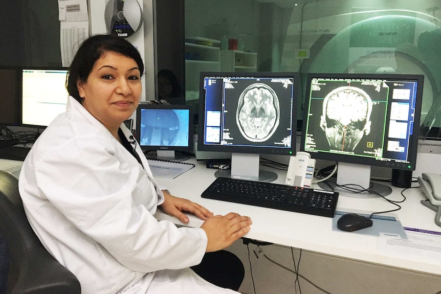 Queensland Brain Institute Researcher Dr Fatima Nasrallah sits in front of MRI scans