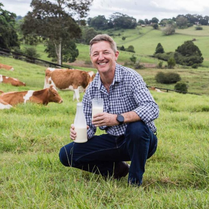 Jeff Hastings in a field of cows holding a glass of milk