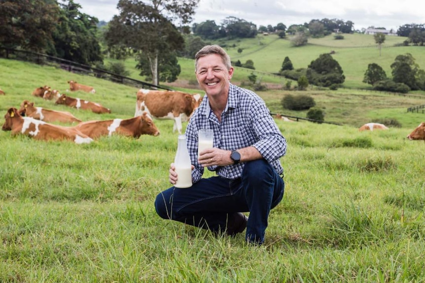 Jeff Hastings in a field of cows holding a glass of milk