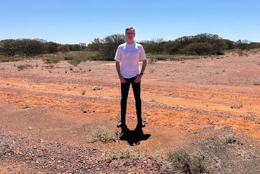 A man stands with his hands in his pockets while standing on red dirt.