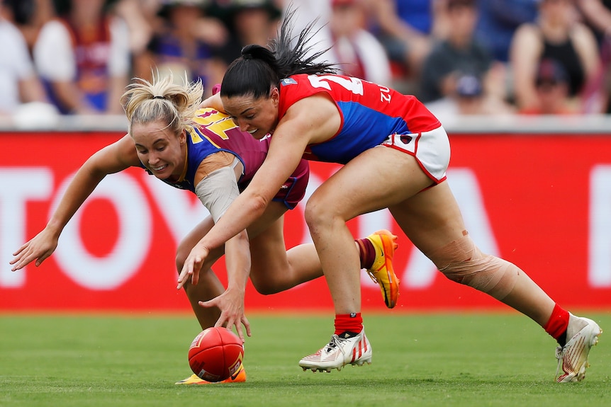 A Brisbane Lions AFLW player contests for the ball alongside a Melbourne opponent.