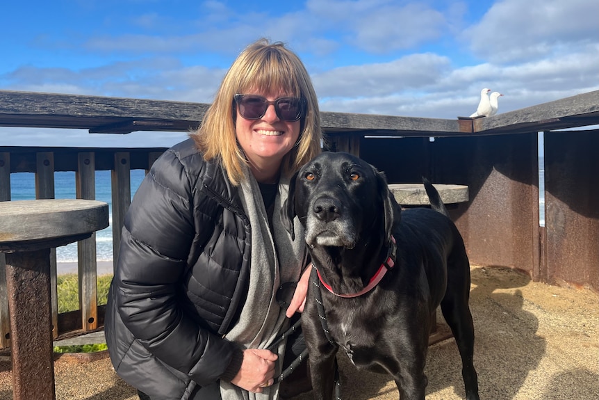 Woman wearing sunglasses next to black dog.