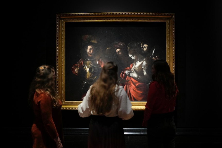 People gather around a hung Caravaggio painting