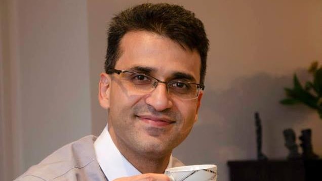 Seyyed Abdolzadeh Ali Farshchi dressed in shirt and tie with a cup of tea and cake.