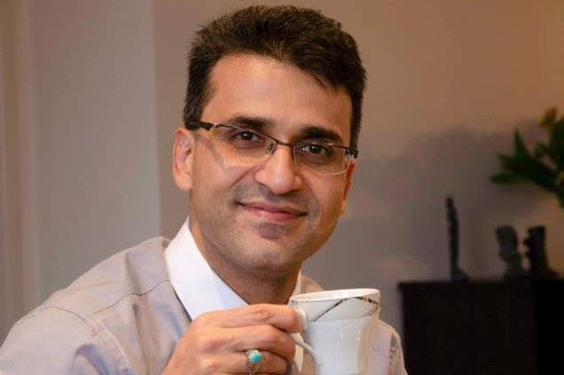 Seyyed Abdolzadeh Ali Farshchi dressed in shirt and tie with a cup of tea and cake.