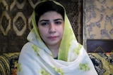 A grainy screenshot from a video call, a woman in a hijab looks into the camera.