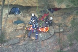 Rescue team helps man as he lays in stretcher on side of cliff