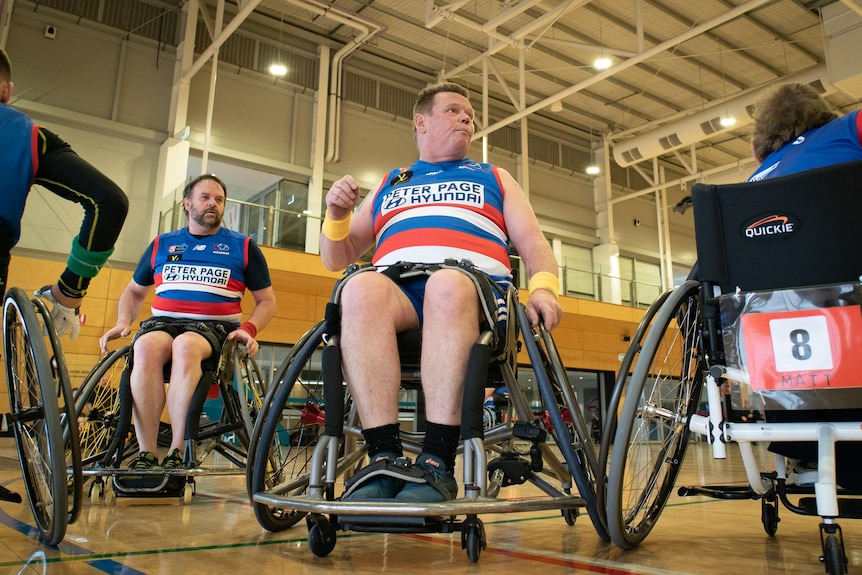 A man in a wheelchair wearing a football guernsey speaks to team-mates