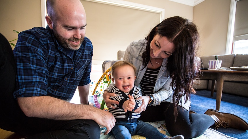 Proud parents Josh and Sallie Koenig sitting on the loungeroom floor with their son Oskar.