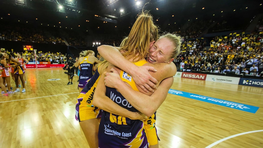 Three lighting players celebrate their win in the Netball Grand Final hugging just after the match has finished