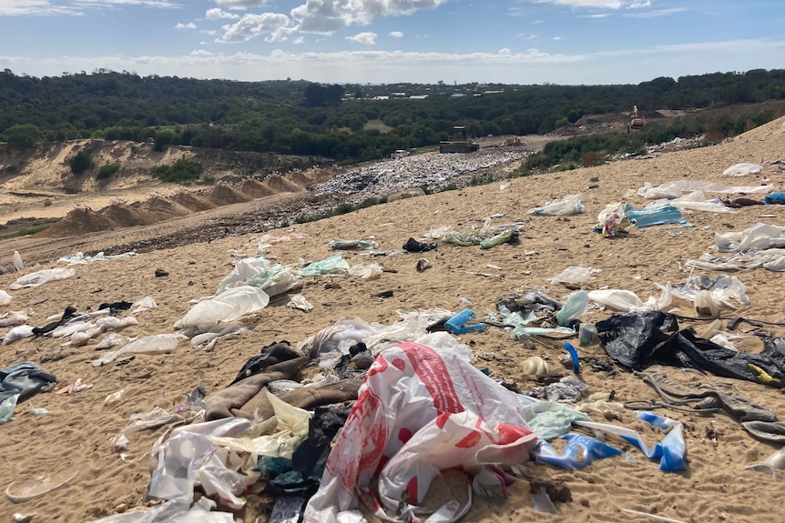 Rubbish is strewn across the sandy ground at a tip.