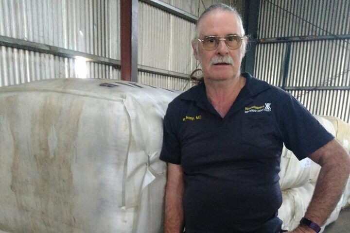Wool classer Anthony Ryan standing next to a bale of wool in a shed.