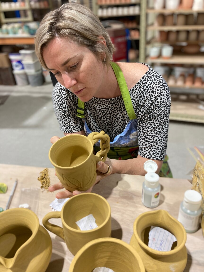 A woman with short blonde hair holding a ceramic mug with a look of deep concentration.