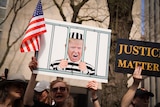 A person holds a poster with a picture of Donlad Trump behind bars