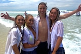 Three girls in wet white t-shirts standing around a tall young boy with an open t-shirt while standing in the ocean