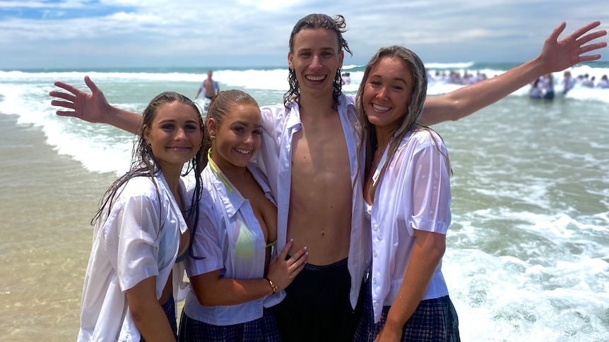 Three girls in wet white t-shirts standing around a tall young boy with an open t-shirt while standing in the ocean