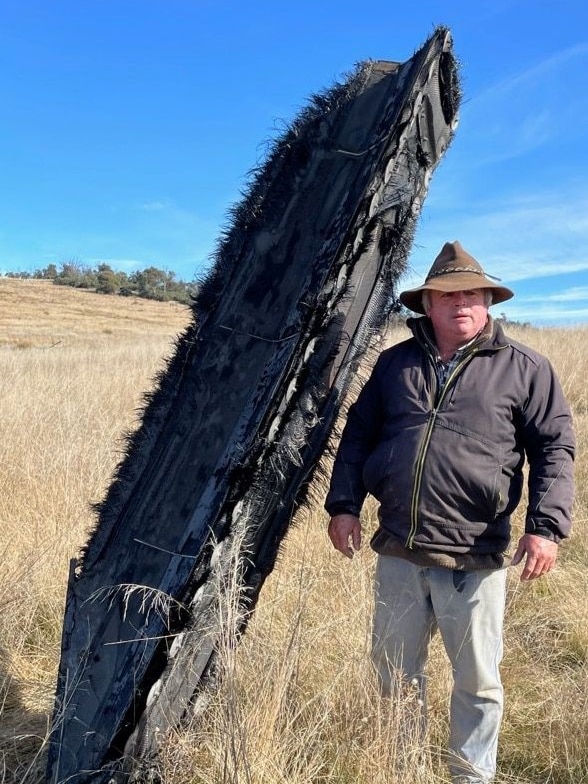 A man stands next to a piece of space junk in a paddock. 