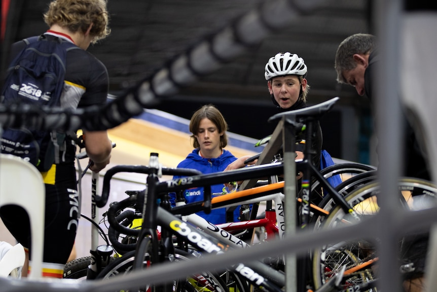 Teenage boys stand huddled around a rack of bicycles.