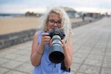 Margaret smiles as she holds a camera with a long lens up to her face.