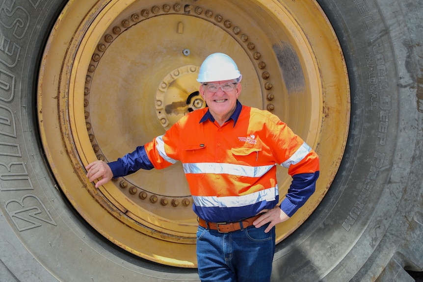 Ian Macfarlane in a hard hate and hi vis standing in front of a huge tyre.