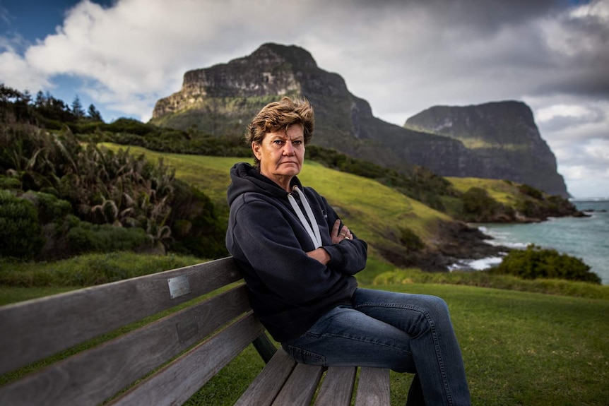 A woman sitting on a bench, frowning at the camera.