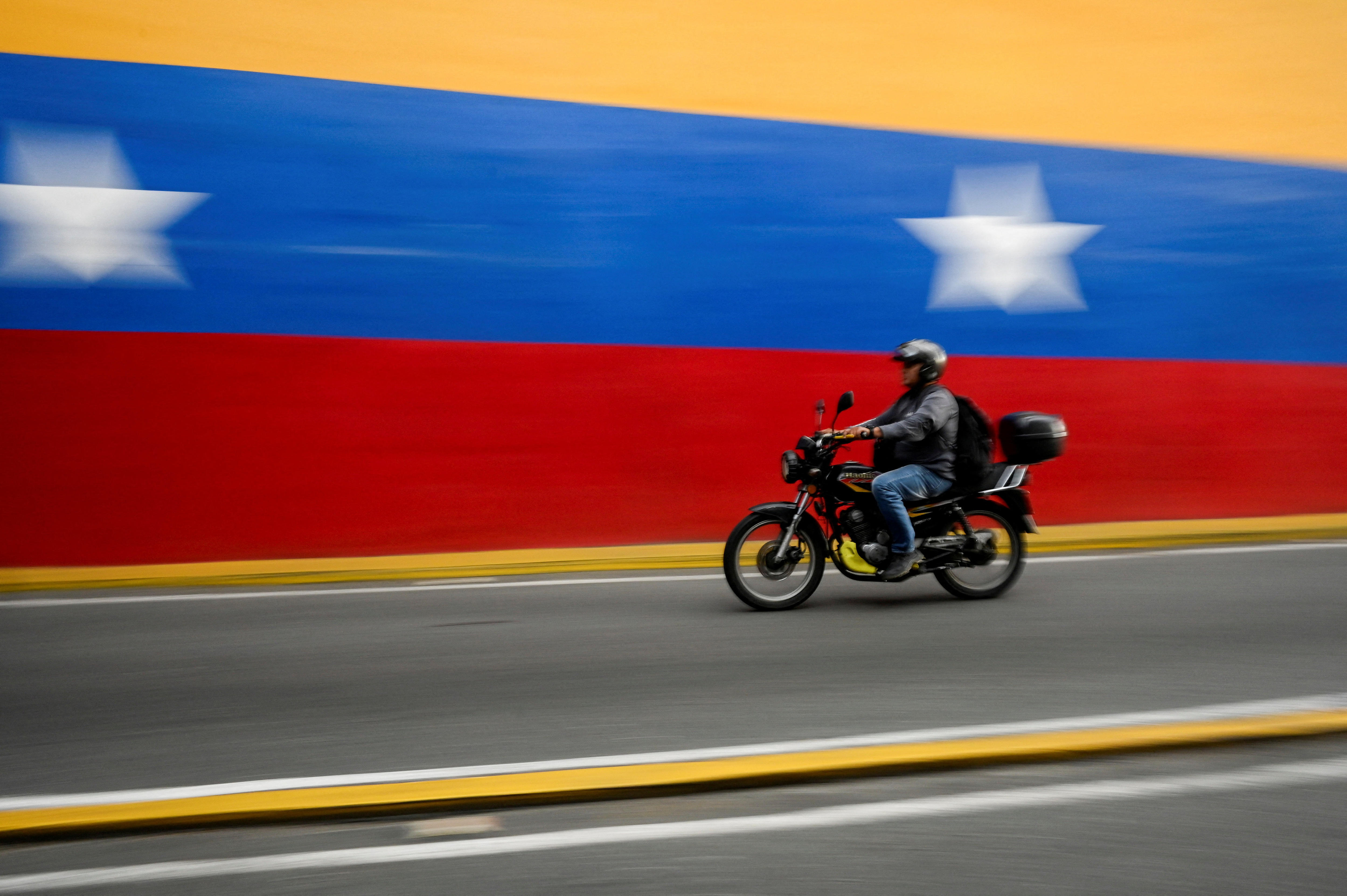 Un hombre pasa una scooter junto a una bandera pintada en la pared.