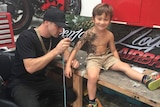 Benjamin Lloyd airbrushes a sleave tattoo on a child.