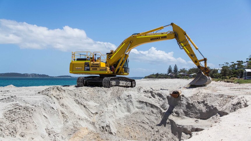 An excavator sits on a sand dune.