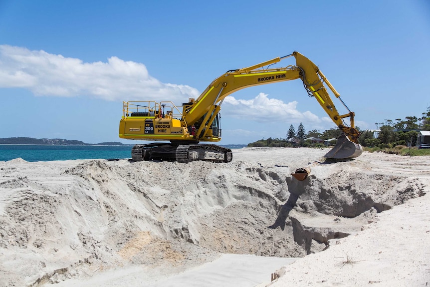 An excavator sits on a sand dune.