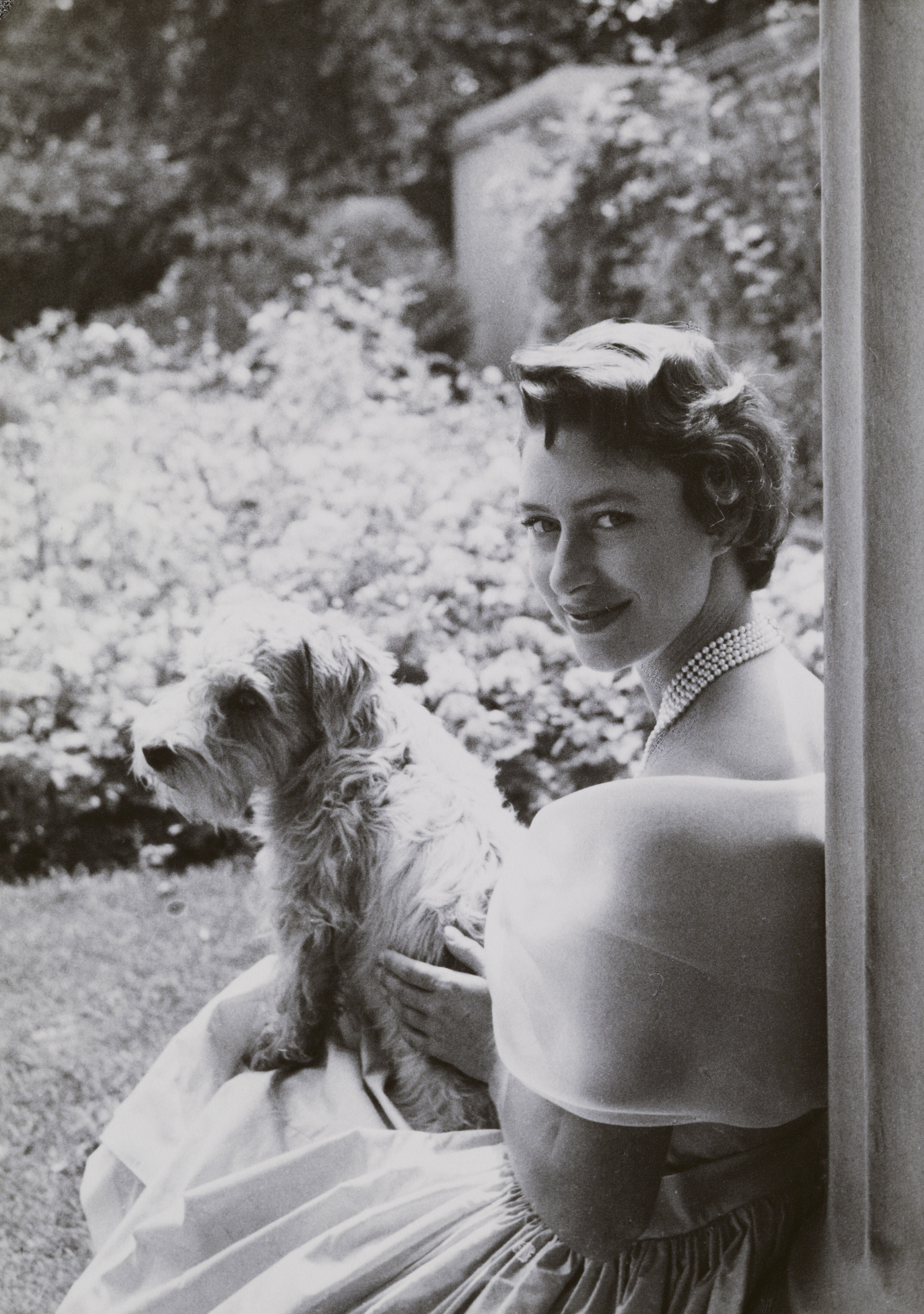 A black and white 25th-birthday portrait of Princess Margaret with her dog Pippin in her lap