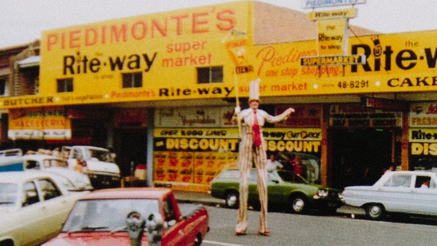 An image of the front of Piedimonte's Supermarket in the 1970s with a man on stilts in a tall top hat.