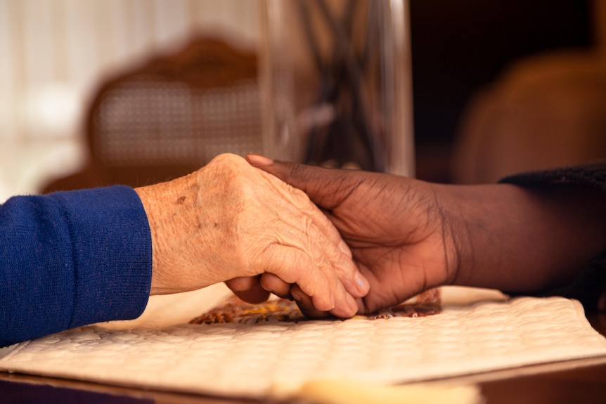 The hand of an elderly person and a younger person holding hands on a table.