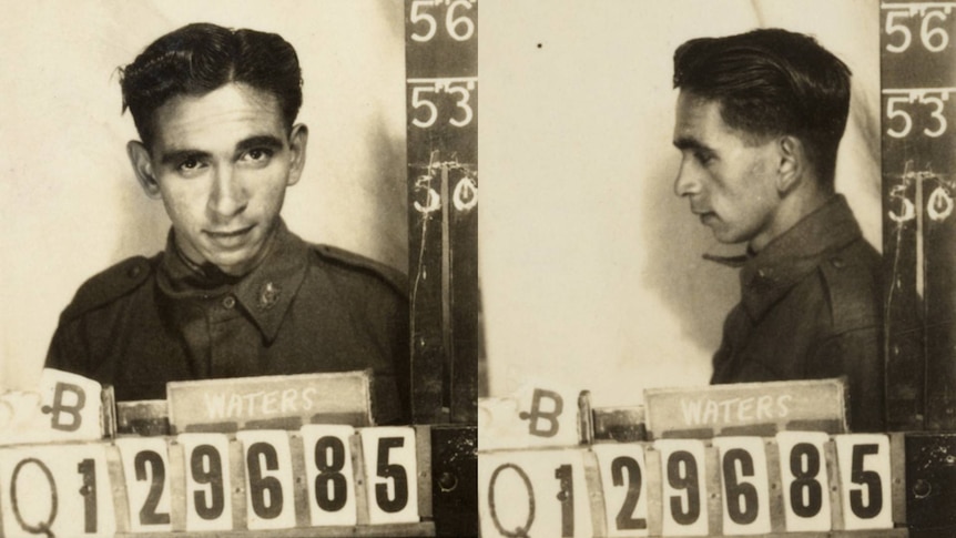 A black and white mug shots of man looking directly at camera & away. He's in uniform, holding a sign saying 'Q129685'.