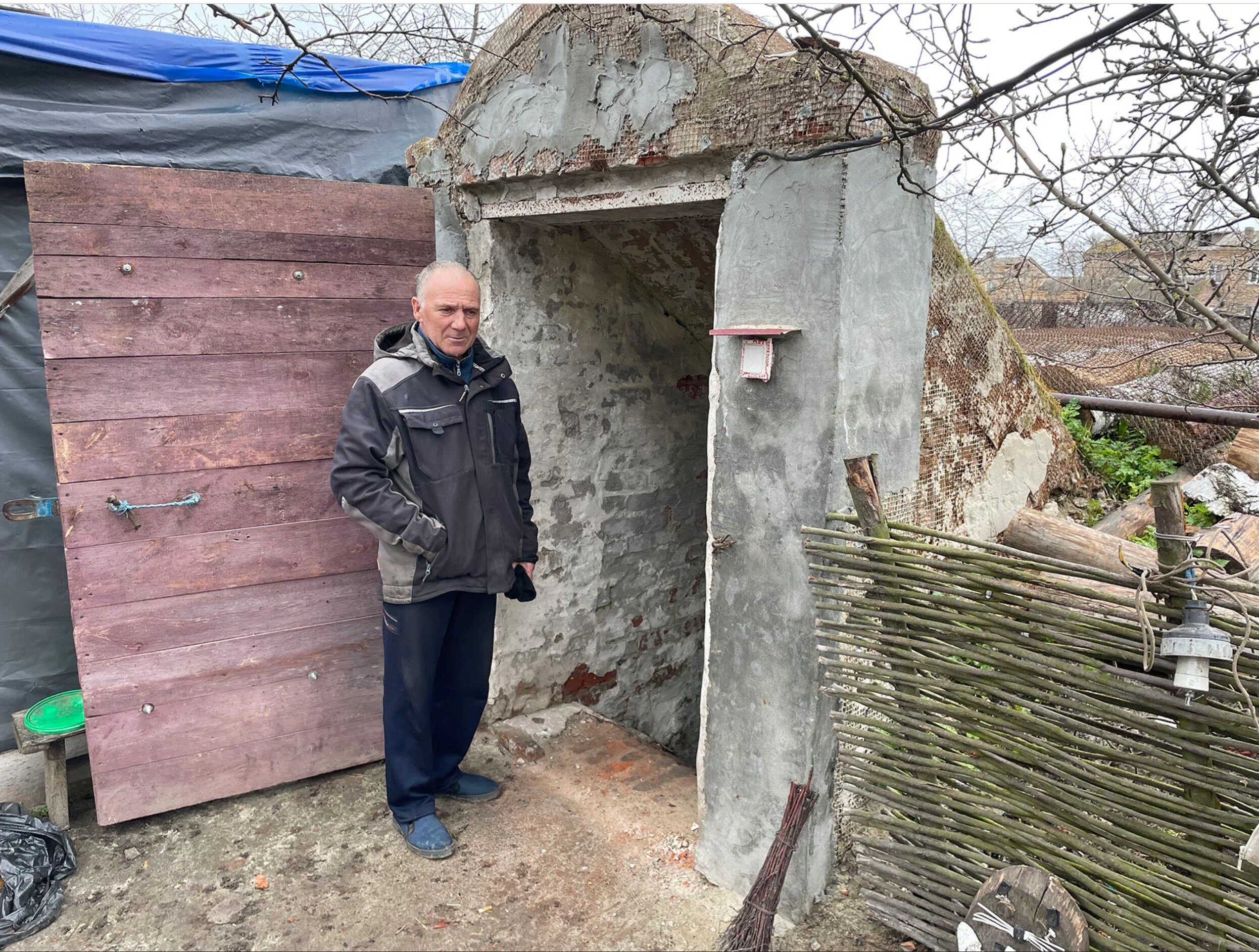 A man stands at the concrete outdoor entrance to a basement. 