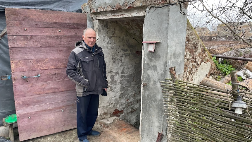 A man stands at the concrete outdoor entrance to a basement. 