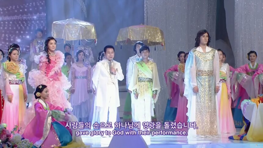 Manmin Central Church founder, Lee Jae-rock in a white suit surrounded onstage by supporters in elaborate traditional costumes.