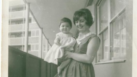 Black and white photograph, a woman stands outside her apartment holding a baby.