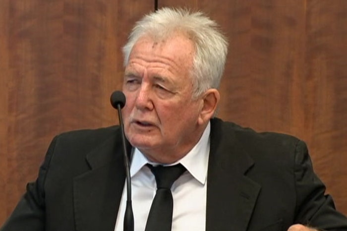 John Woodman sits in a chair in front of a microphone against a wooden wall as he testifies at the IBAC hearing in Melbourne.