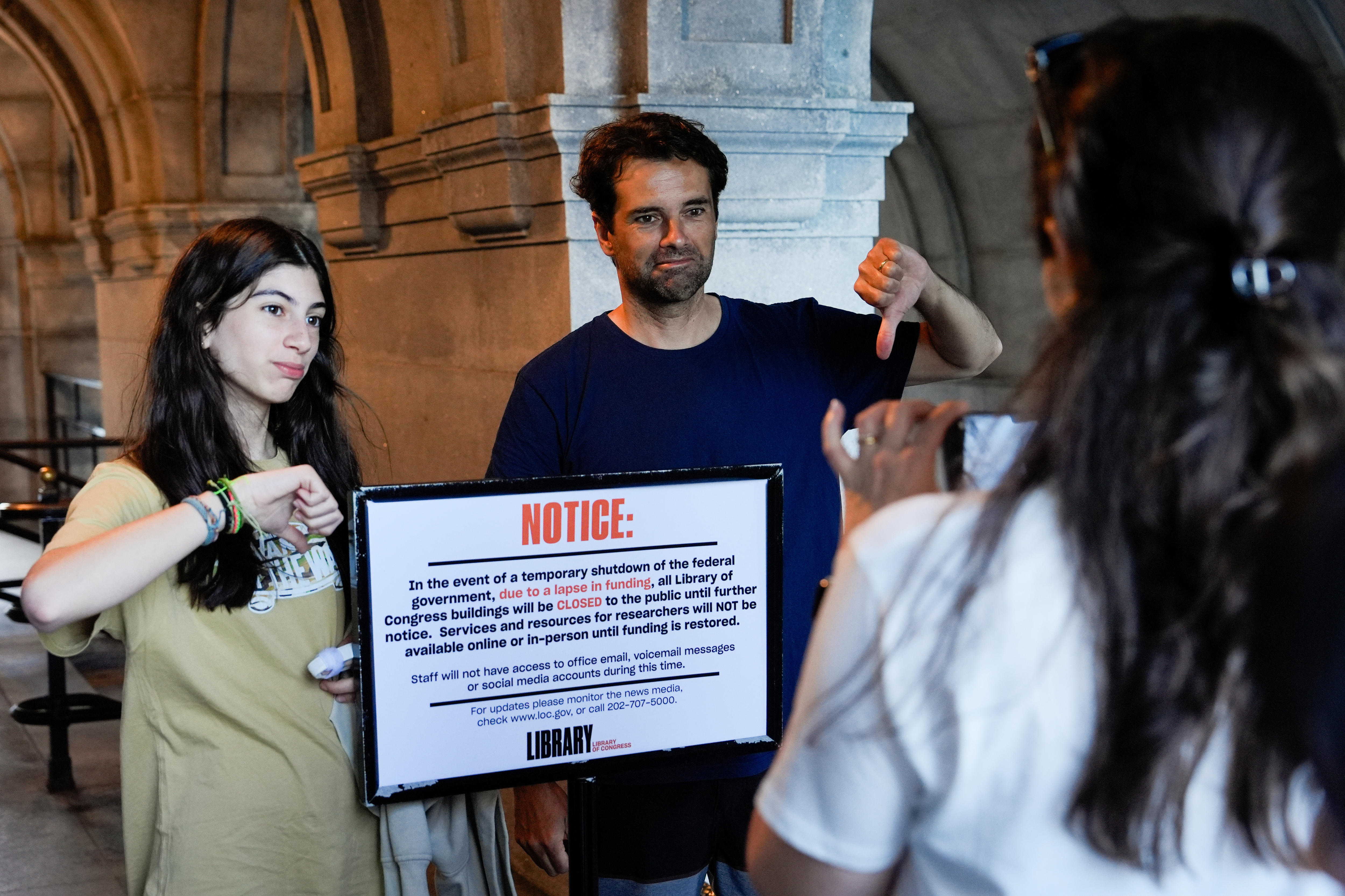 A man and woman give the thumbs-down behind a closed sign in a grand building.