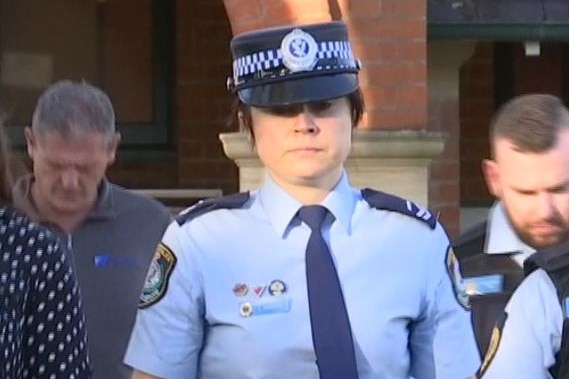 A police offier in uniform leaving court flanked by a sherrif
