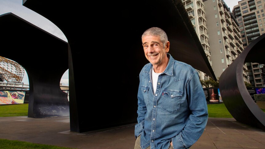 Trevor Chappell standing in front of big black arching sculptures in Melbourne.