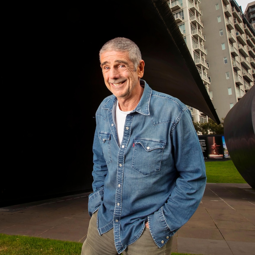 Trevor Chappell standing in front of big black arching sculptures in Melbourne.