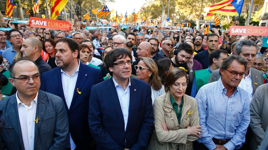 Carles Puigdemont stands with other leaders at the front of a large group of people.