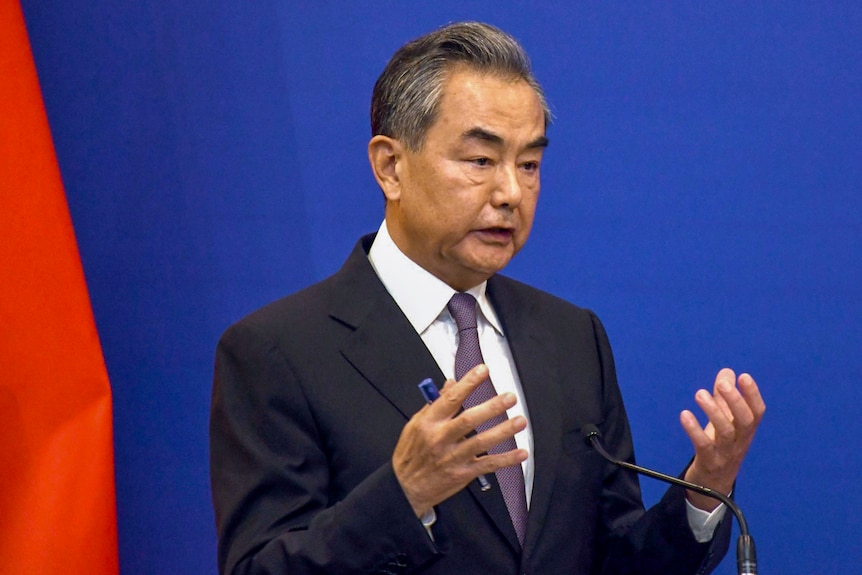China's foreign minister gestures with blue background. 