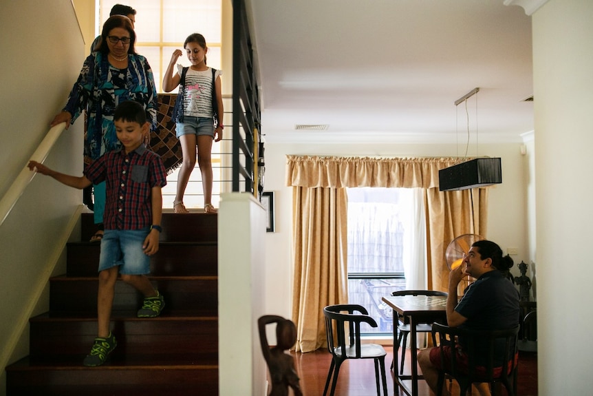 Four people walk down a flight of stairs while a man sitting at a table looks on.