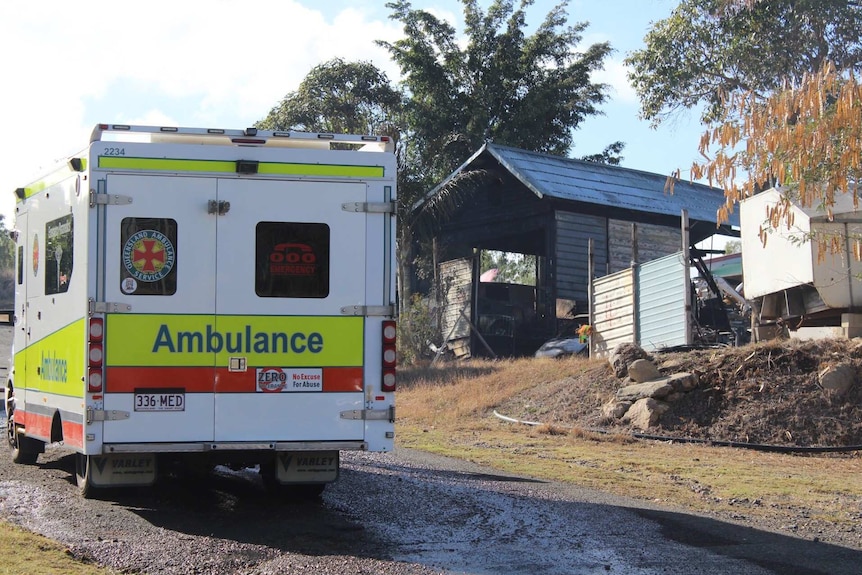 An ambulance outside a shed and house destroyed by fire.