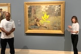 A man and a woman stand either side of a gold-framed painting of a man sitting in the bush with a yellow Woodside logo on it